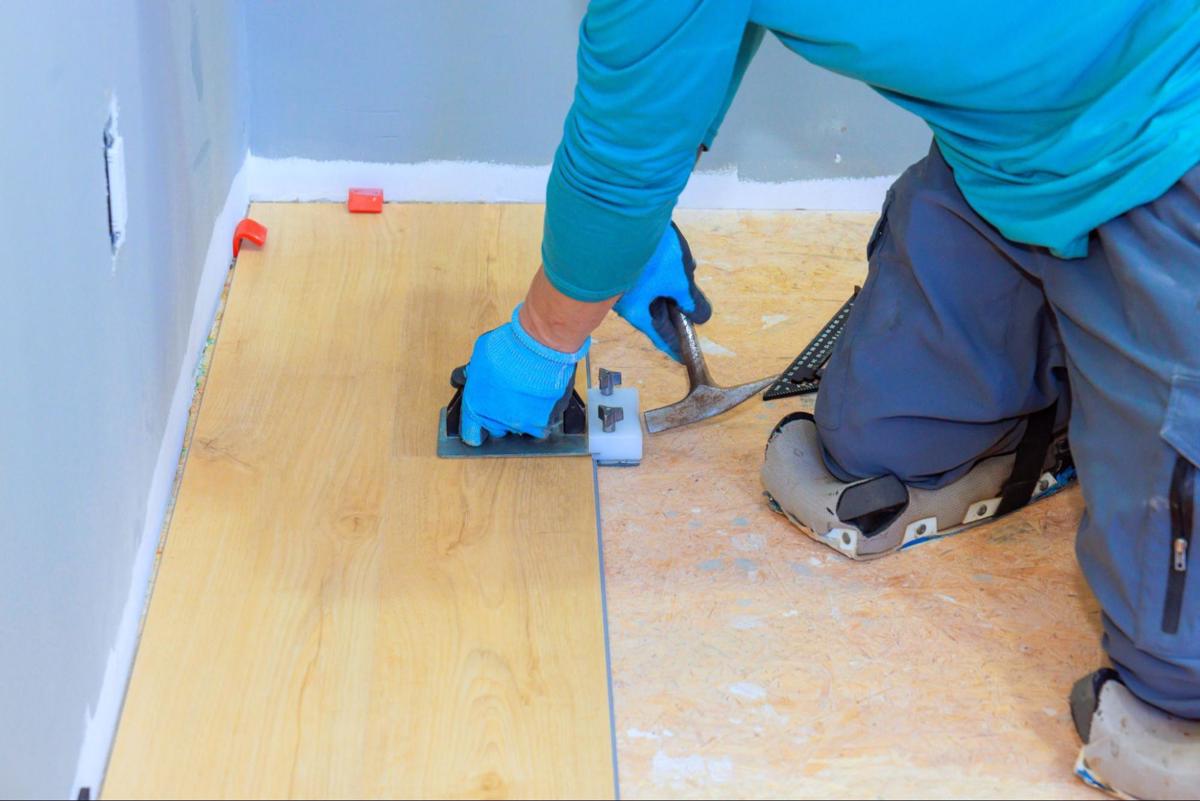Vakman plaatst klikvinyl plank met slagblok en hamer op een houten ondervloer.